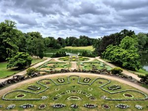 Blick auf ein Blumenparterre eines Schlossgartens, im Hintergund hohe Bäume